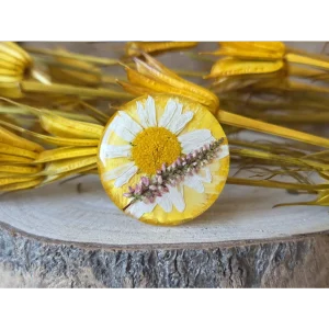 Broche circular amarillo con pétalos de rosa, margarita y ramitas de brezo en resina transparente. Joyería botánica L’atelier d’Aaron.