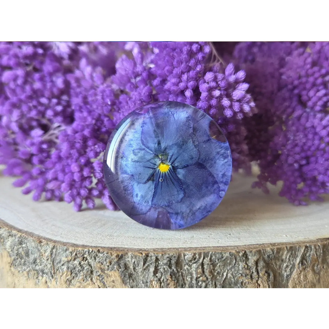 Broche redondo azul con flor de pensamiento y viola encapsuladas en resina artesanal.