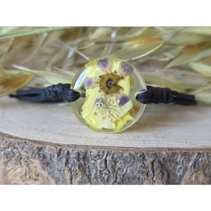 Pulsera amarilla con clavel, flor de cera y amimaju en resina transparente sobre base de madera