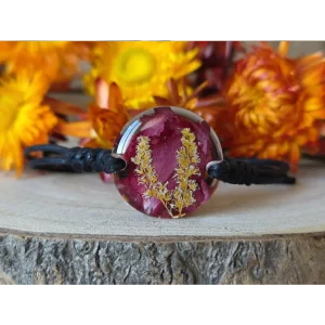 Pulsera burdeos con clavel y astilbe japónica natural encapsulada en resina, sobre fondo de flores secas naranjas