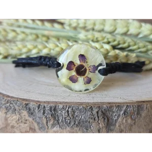 Pulsera crema con clavel y flor de cera en resina transparente sobre base de madera